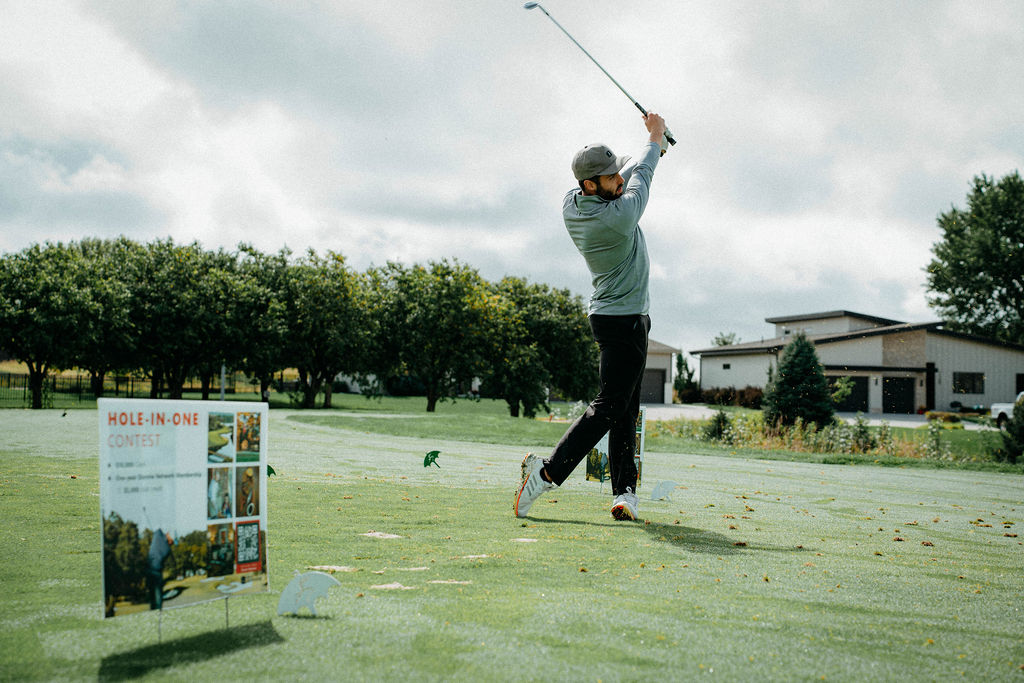 Golfer mid-swing beside the hole-in-one contest sign