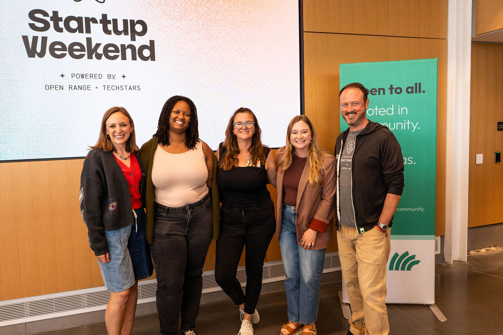 Organizers smiling in front of the Startup Weekend screen
