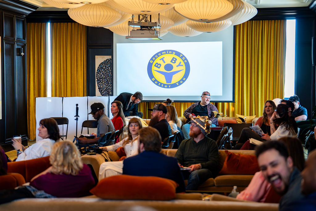 Audience seated in a lounge-style room with the BTBY logo on screen